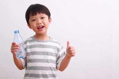cute little asian boy showing thumb up sign with a bottle of water isolated on white background