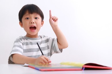 smart little asian boy having an idea while doing his homework, isolated on white background