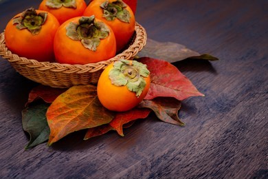 persimmon fruits in basket and persimmon colored leaves on wooden background, top view.