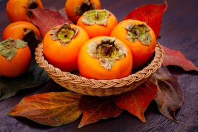 persimmon fruits in basket and persimmon colored leaves on wooden background, top view.