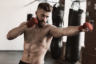 athletic male boxer training at boxing studio. portrait of muscular bearded man during exercise. sporty man during boxing exercise making direct hit. strength and motivation concept