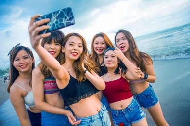 lifestyle beach portrait of asian korean and chinese women, group of happy beautiful young girlfriends taking selfie picture together with mobile phone smiling cheerful enjoying girls holidays trip