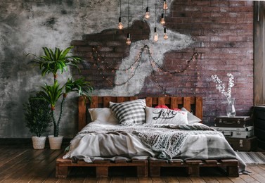 stylish bedroom in loft style with lots of pillows and lots of light bulbs. bed on brick wall background. modern loft bedroom design.