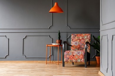 bright orange ceiling light above a boho style armchair in an elegant living room interior with molding on gray walls and copy space place for a chair. real photo.