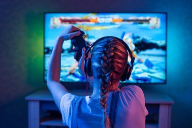 a gamer or a streamer girl at home in a dark room with a gamepad playing with friends on the networks in video games. a young man sits in front of a monitor or tv.
