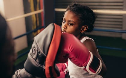 close up of a kid training inside a boxing ring. kid boxer wearing boxing gloves practicing punches on a punching pad.
