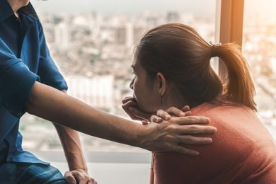 psychologist sitting and touch young depressed asian woman for encouragement near window with low light environment, selective focus, ptsd mental health concept,