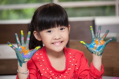 cute asian little girl with hands in paint , in classroom school  concept - happy children showing painted hand palms at preschool . early education . kid in kindergarten . intelligence
