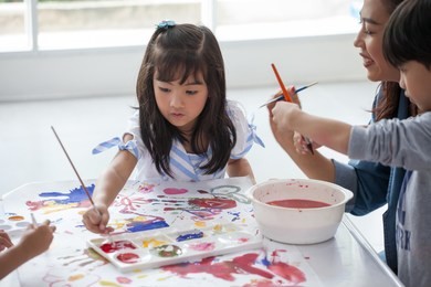 group of cute little girl student painting  together with nursery teacher in classroom school . happy children in a kindergarten