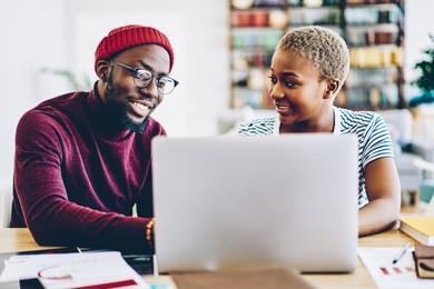 african american couple browse website on laptop computer making shopping online together at home interior, positive dark skinned hipster guy showing new app for netbook sitting at his girlfriend