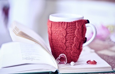 white cup with the red knitted thing on it staying on the open book