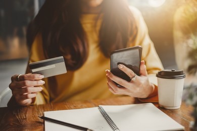 young beautiful asian woman using smart phone and credit card for shopping online in coffee shop cafe, vintage tone color