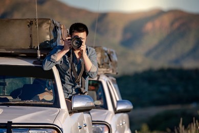 young asian male traveler and photographer sitting on the car window taking photo on road trip in namibia, africa. travel photography concept