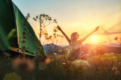 happy woman with open arms stay near tent around mountains under sunset light sky enjoying the  leisure and freedom.