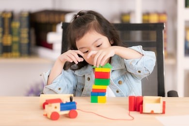lovely cute little asian girl in jeans shirt concentrate  playing wood block toys on desk. concept for funny activity of young kids in free time.