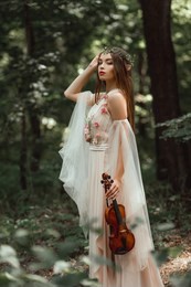 mystic elf in flower dress and floral wreath holding violin in forest