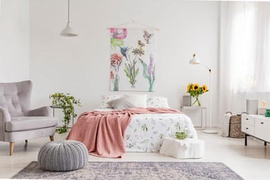 nature lover's bright bedroom interior with a wall art of flowers and birds painted on a fabric above a bed which is dressed in green plants pattern on white linen. real photo.
