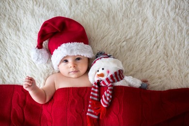 christmas portrait of cute little newborn baby boy, wearing santa hat and hugging little cute snowman toy, studio shot, winter time