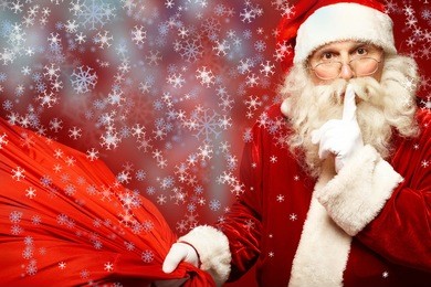 portrait of santa claus with huge red sack keeping forefinger by his mouth and looking at camera