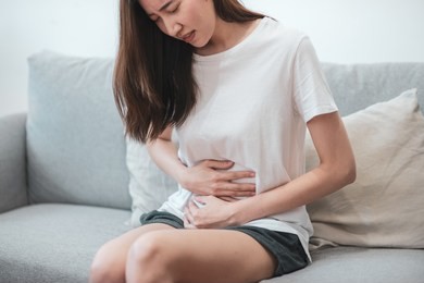 healthcare medical or daily life concept : close up stomach of young lady have a stomachache or menstruation pain sitting on a sofa.