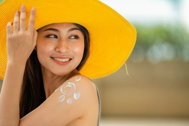 attractive asian woman in yellow hat with healthy skin applying sunscreen standing outdoors on a sunny day.