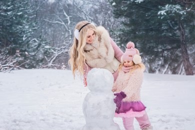 mom and little daughter dressed in pink clothes have fun and make a snowman in a snowy park