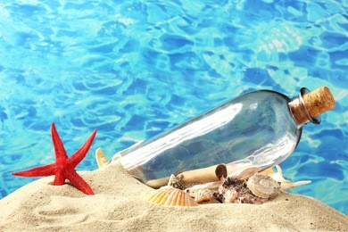 glass bottle with note inside on sand, on blue sea background