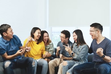 young attractive asian group of friends talking and laughing with happy in gathering meeting sitting at home feeling cheerful and enjoy game in leisure time together. people in blue or yellow wearing.