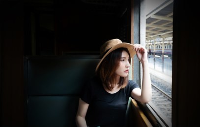 attractive young woman passenger sitting inside train and looking through window. teenage girl wearing hat feels lonely and looking outside the train window.