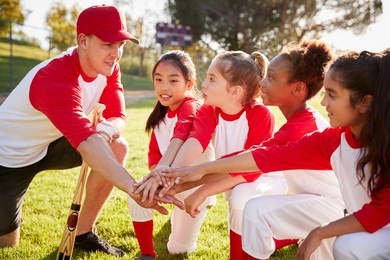 girl baseball team kneeling with their coach, touching hands