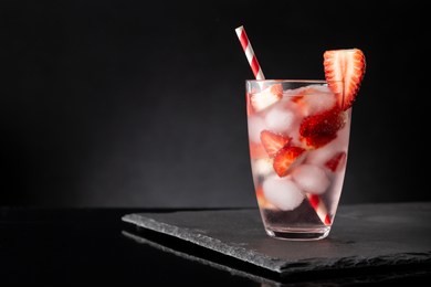 glass of cold infused water with fresh strawberry slices on a black stone tray