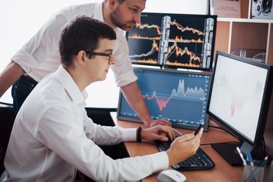 businessmen trading stocks online. stock brokers looking at graphs, indexes and numbers on multiple computer screens. colleagues in discussion in traders office. business success concept.