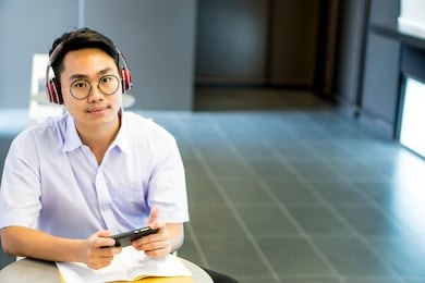 asian happy cute young boy student study in school library he using smartphone wearing headphones play game or learning lesson online class room exam back to school education concept have copy space