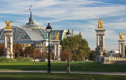 view of grand palais and golden statues at pont alexandre iii bridge. french flag waves on top of the building. paris, france.