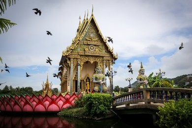 the thai temple in wat plai laem in samui island thailand, in the middle of the water, contains giant statues and elephants.pigeon flies through.