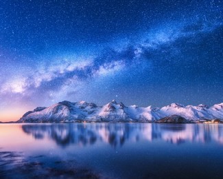 bright milky way over snow covered mountains and sea at night in winter in norway. landscape with snowy rocks, starry sky, reflection in water, fjord. lofoten islands. space. beautiful milky way
