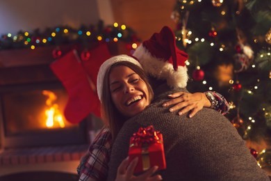 young couple in love sitting by the fireplace and nicely decorated christmas tree, exchanging christmas presents