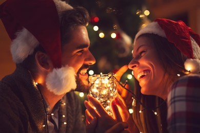 young couple in love sitting by the fireplace and nicely decorated christmas tree, enjoying the christmas magic. focus on the man