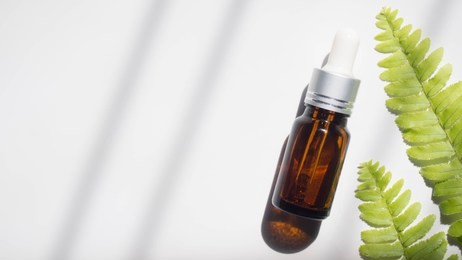 natural beauty cosmetic product for skincare concept. brown glass vial w/ dropper and organic green leaves on white background. serum or essential oil w/ herbal extract. branding mock-up. copy space.