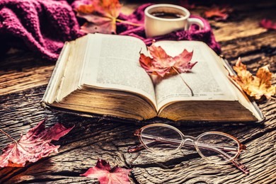 cup of coffee old  book  glasses and autumn leaves on rustic wooden table.