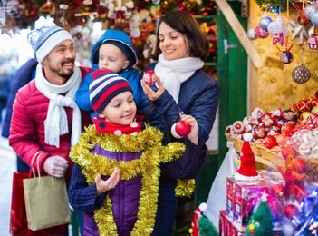 ordinary cheerful  parents with kids choosing x-mas decorations in market
