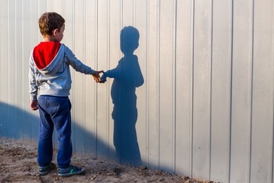 boy and his shadow. lonely little child playing with his shadow outside. the concept of autism and loneliness. copy space for your text