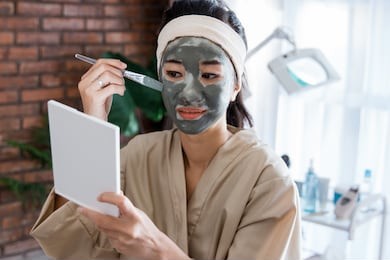young woman using facial mask mud herself at home