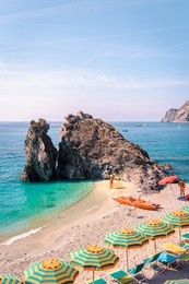 young woman on the beach walking with red dress and hat, chairs and umbrellas fill the spiaggia di fegina beach , the wide sandy beach village of monterosso italy, part of the cinque terre italy