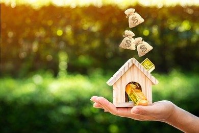 woman show hand holding a model home and gold bar and dropping a money bag on sunlight in the public park, saving money for buy a new house or loan for plan business investment of real estate concept.