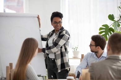 business people at seminar conference sitting in office. black african leader boss female standing show on whiteboard development strategy plan graph to young colleagues clients at business meeting