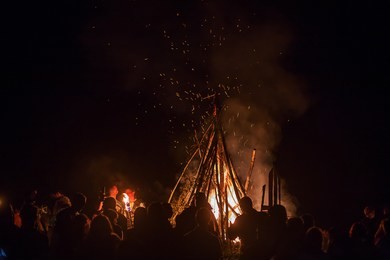 people are happy to have fun and dance in a round dance around a large fire warming them with flame at night at a multicultural ethnic festival, a lot of sparks and heat from burning wood
