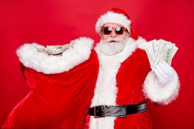 portrait of santa in eyeglasses gloves outfit holding carrying huge sack with currency discount sale lottery win winner congratulations isolated over bright vivid red background