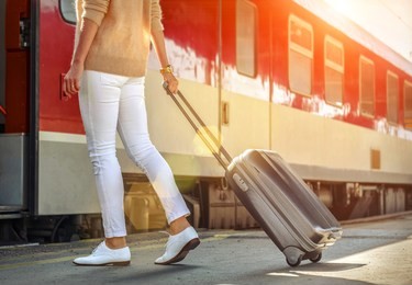 woman with her luggage go  to red train on the peron of rail station under sun light at sunny day.