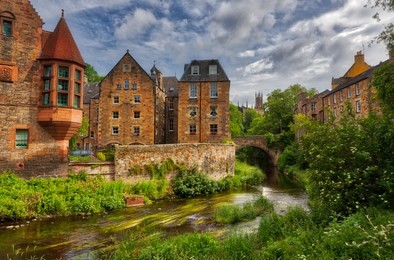 quaint stream with green flora along it flowing through dean village in edinburgh with old scottish buildings